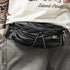 Person wearing a black waist bag with visible branding on a neutral background